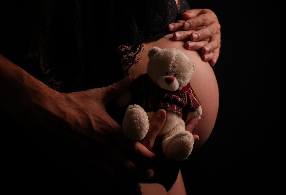 Mains et ourson en peluche posés sur un ventre de femme enceinte